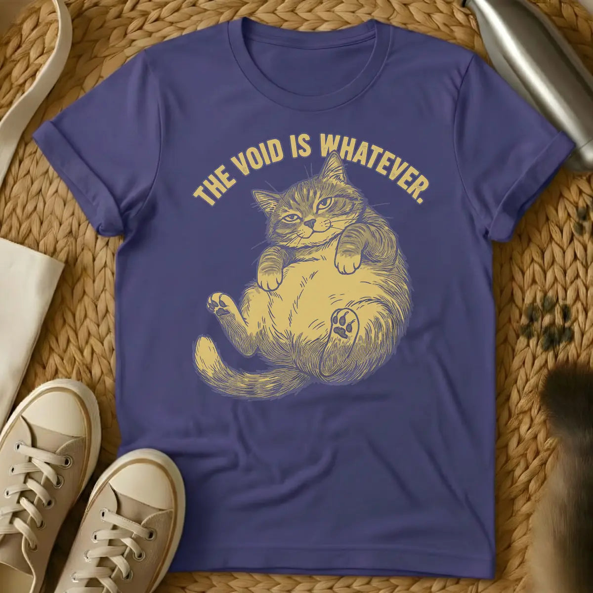 Purple - Distressed, gold-colored, linocut-style illustration of a cat lying on its back with its belly and one paw pad exposed, giving an indifferent look. Above, arched text reads 'THE VOID IS WHATEVER.'