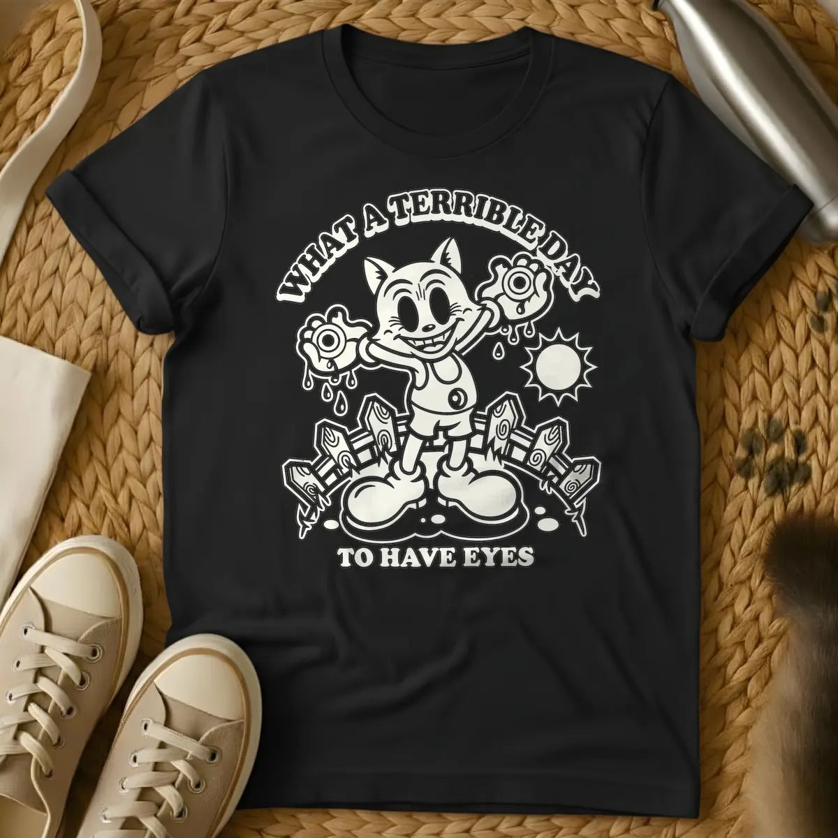 Black - Cream retro cartoon character, resembling a grinning cat with large eyes, holding two dripping eyeballs in its hands. Behind it are a picket fence and a bright sun. Arched text above reads "WHAT A TERRIBLE DAY" and straight text below reads "TO HAVE EYES".