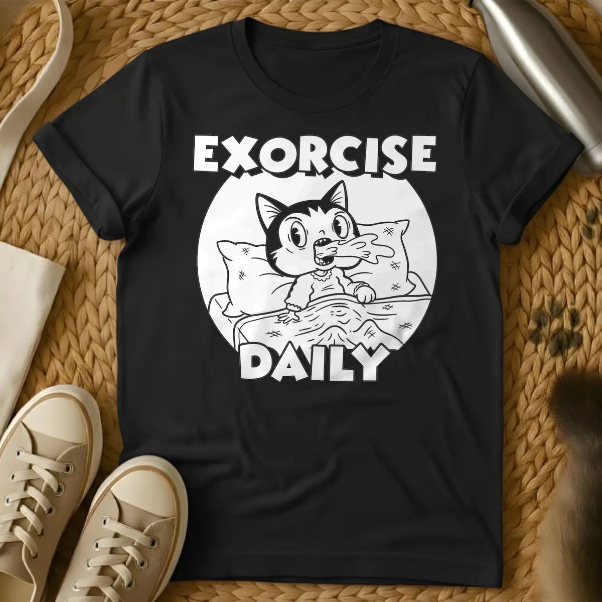 Black - T-shirt design of a cartoon cat sleeping comfortably under a blanket with a pillow. Above the cat is the word 'EXORCISE' and below is 'DAILY'.