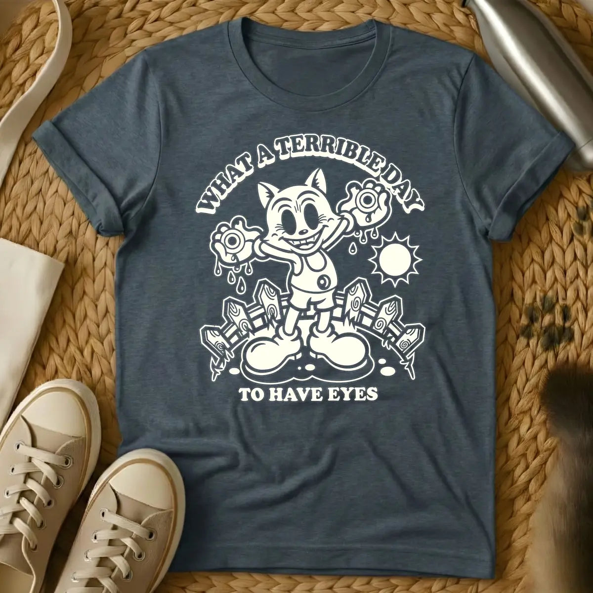 Dark Heather - Cream retro cartoon character, resembling a grinning cat with large eyes, holding two dripping eyeballs in its hands. Behind it are a picket fence and a bright sun. Arched text above reads "WHAT A TERRIBLE DAY" and straight text below reads "TO HAVE EYES".