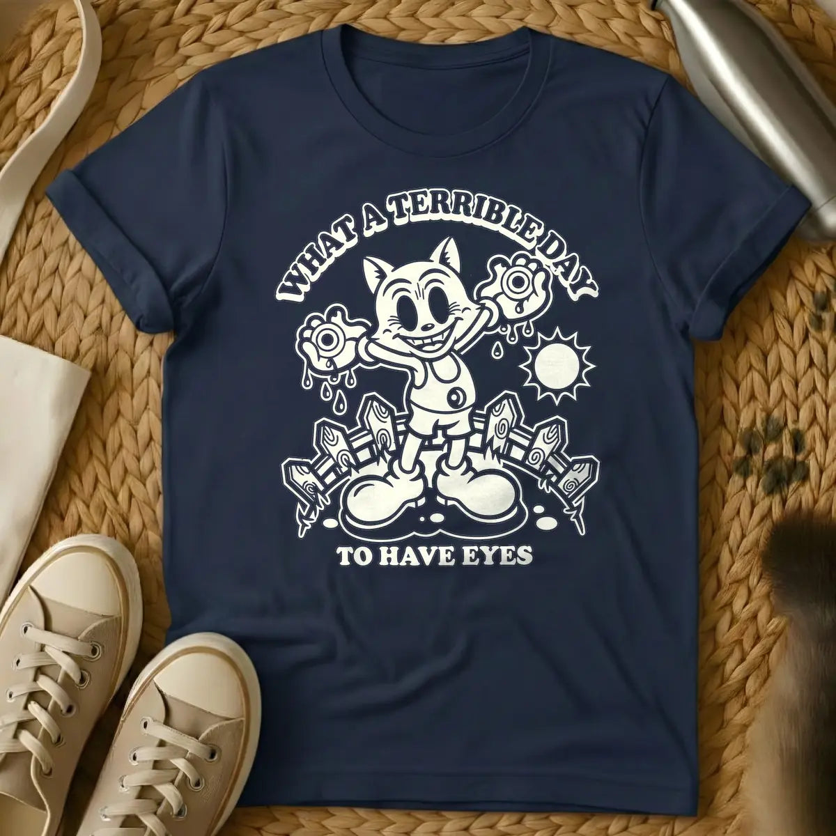 Navy - Cream retro cartoon character, resembling a grinning cat with large eyes, holding two dripping eyeballs in its hands. Behind it are a picket fence and a bright sun. Arched text above reads "WHAT A TERRIBLE DAY" and straight text below reads "TO HAVE EYES".