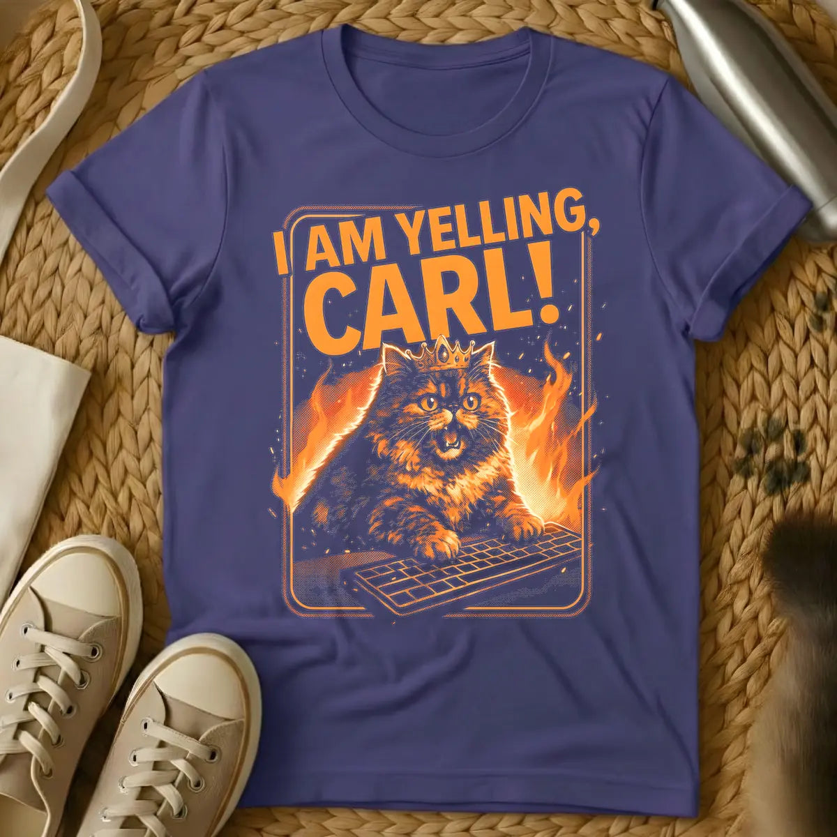 Purple - Orange and black t-shirt design featuring a crowned, angry-looking cat with wide eyes and an open mouth, surrounded by flames, aggressively typing on a computer keyboard. Above the cat, the bold orange text reads "I AM YELLING, CARL!"